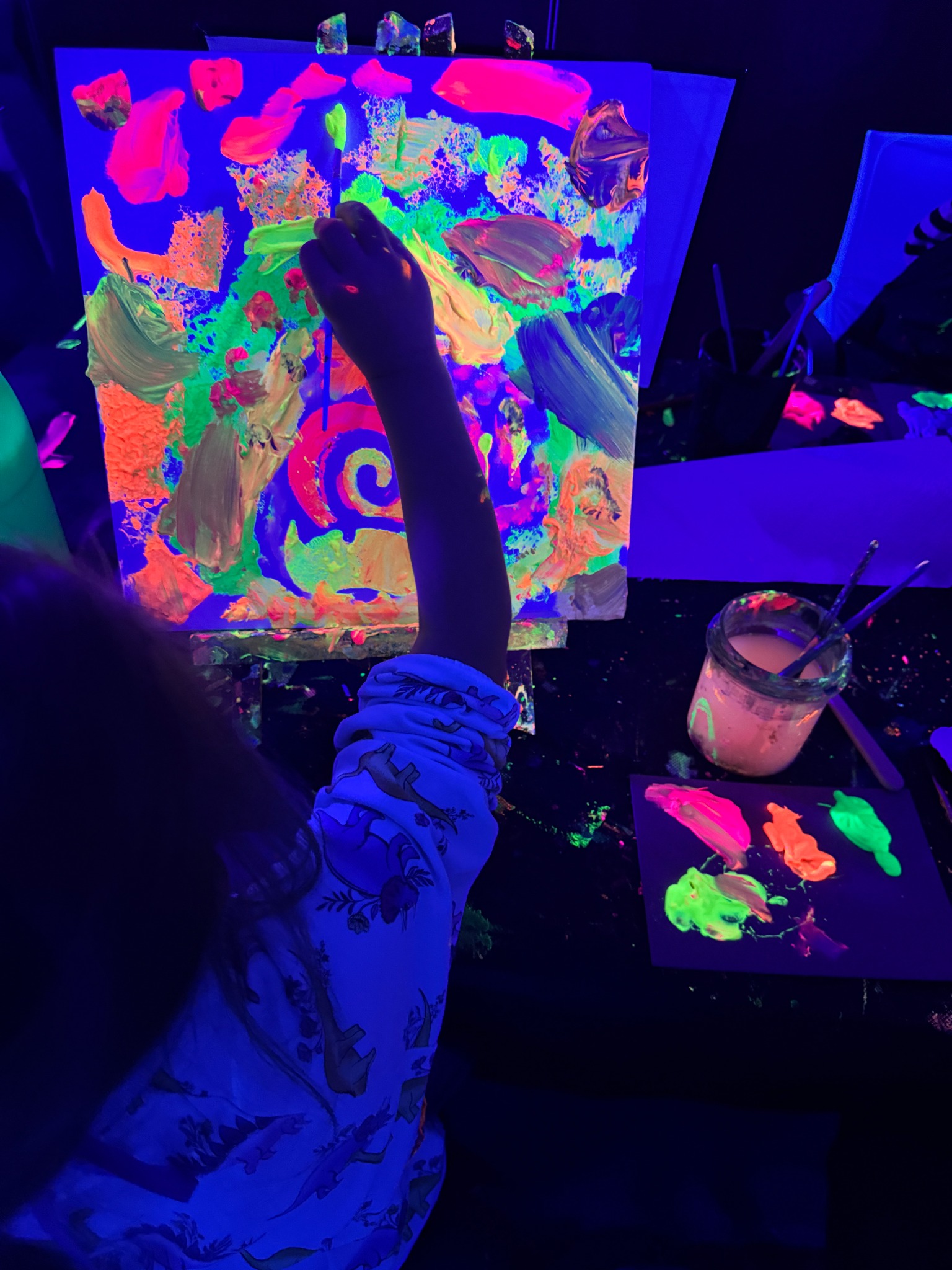 Ein Kind malt mit leuchtenden Neonfarben auf einer Leinwand unter Schwarzlicht.