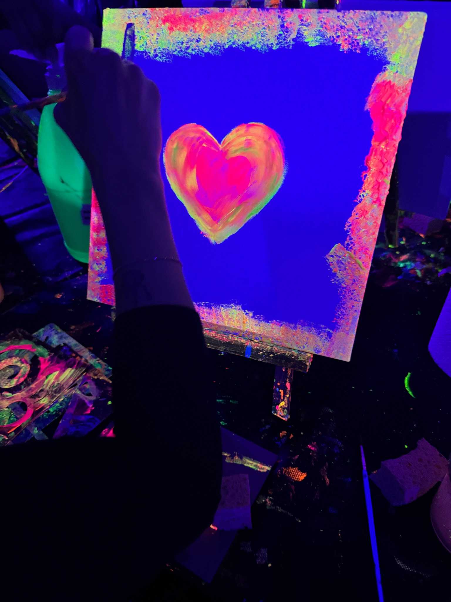 Ein leuchtendes Herz entsteht auf einer Leinwand unter Schwarzlicht.