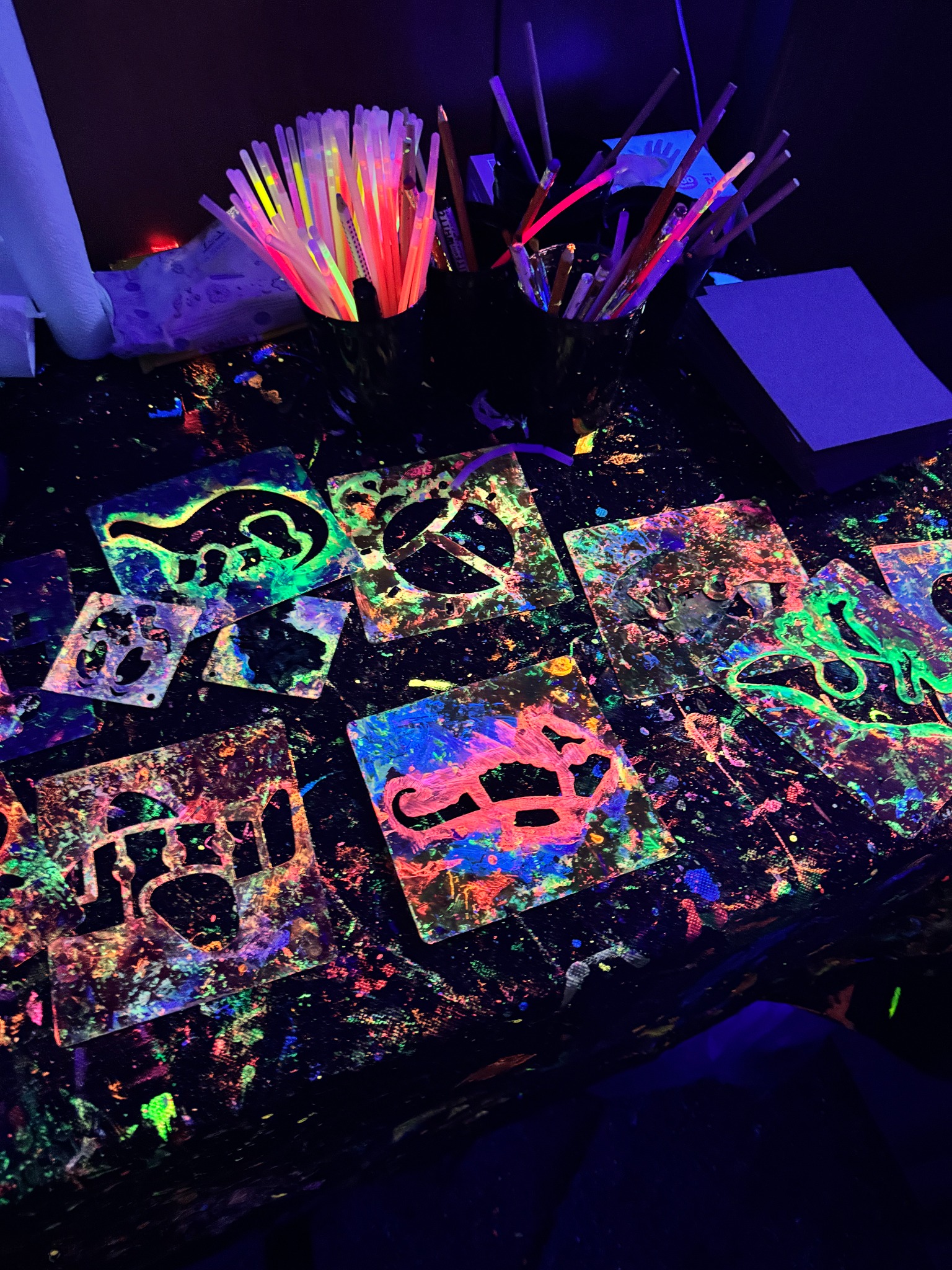 Schablonen und Pinsel auf einem mit Neonfarben besprenkelten Maltisch.