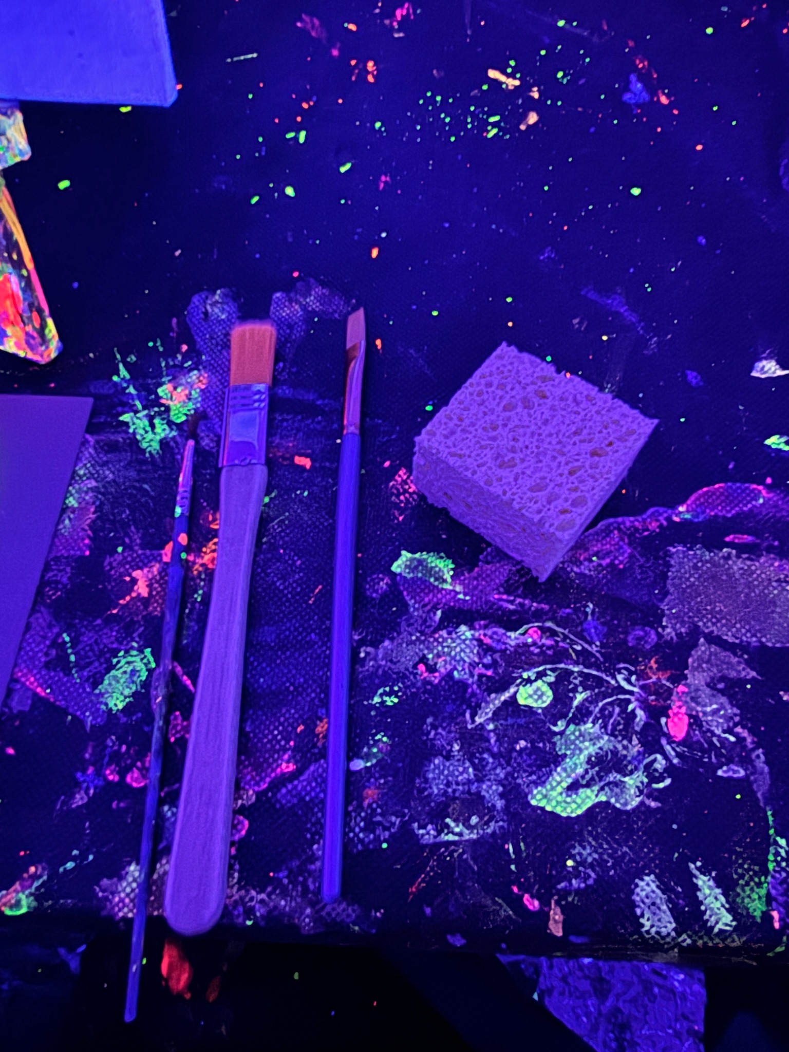 Pinsel und Schwämme auf einem Maltisch unter Schwarzlicht.